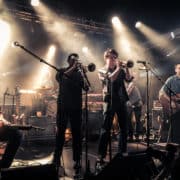 Calexico, 2015-04-25 on stage at "Den Atelier", Luxembourg. From left to right: Jairo Zavala, John Convertino, Jacob Valenzuela, Martin Wenk, Sergio Mendoza, Joey Burns, Ryan Alfred. Auteur: Zippo Zimmerman. (Wikimedia, CC BY-SA 4.0)